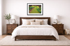 A bedroom with a wooden bed, white bedding, and a black framed artwork on the wall.