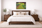 Metal painting of a garden path hanging in a bedroom with a wooden bed, white bedding. 