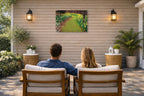 A couple sitting on a patio with outdoor furniture, facing a wall with a scenic painting.