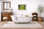 A white-framed wall art image in a bathroom with a freestanding bathtub, wooden cabinet, and decorative elements.