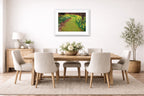 Dining room with wooden table and chairs, white framed artwork on the wall, and decorative plants.